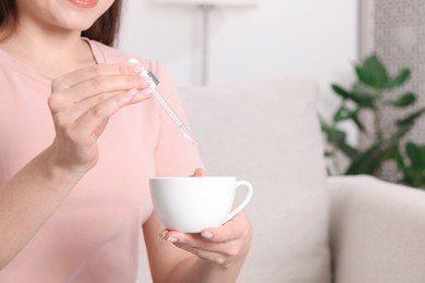 Photo of Woman dripping food supplement into cup indoors, closeup. Space for text