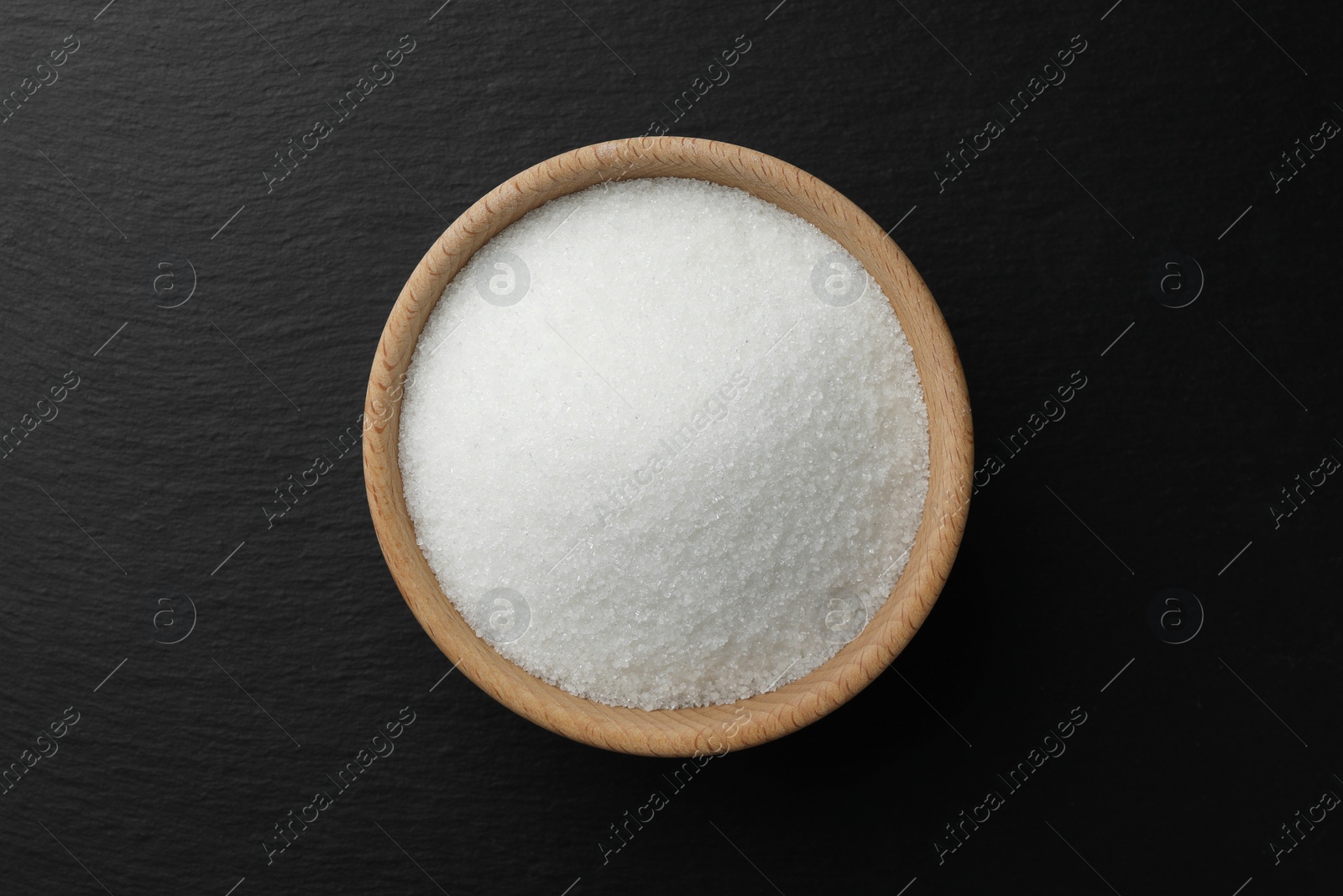 Photo of Granulated sugar in bowl on black table, top view