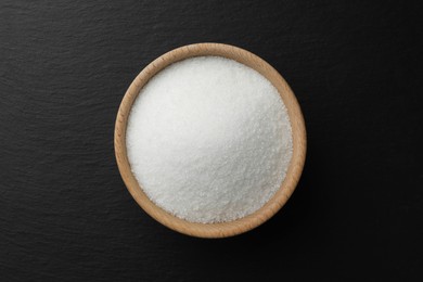 Granulated sugar in bowl on black table, top view