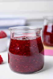 Photo of Delicious raspberry jam in jar on white table, closeup