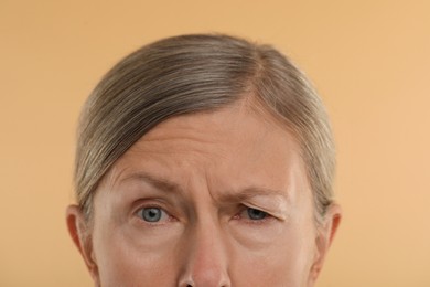 Photo of Woman with wrinkles on her forehead against beige background, macro view