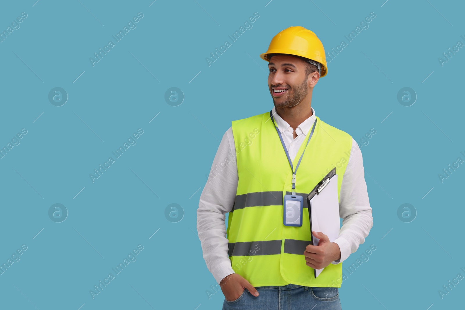 Photo of Engineer in hard hat holding clipboard on light blue background, space for text