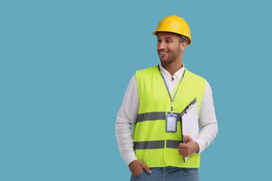 Engineer in hard hat holding clipboard on light blue background, space for text
