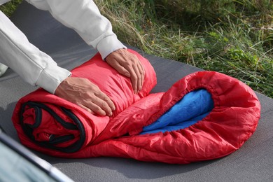 Photo of Woman folding red sleeping bag outdoors, closeup