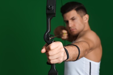 Man with bow and arrow practicing archery against green background, focus on hand