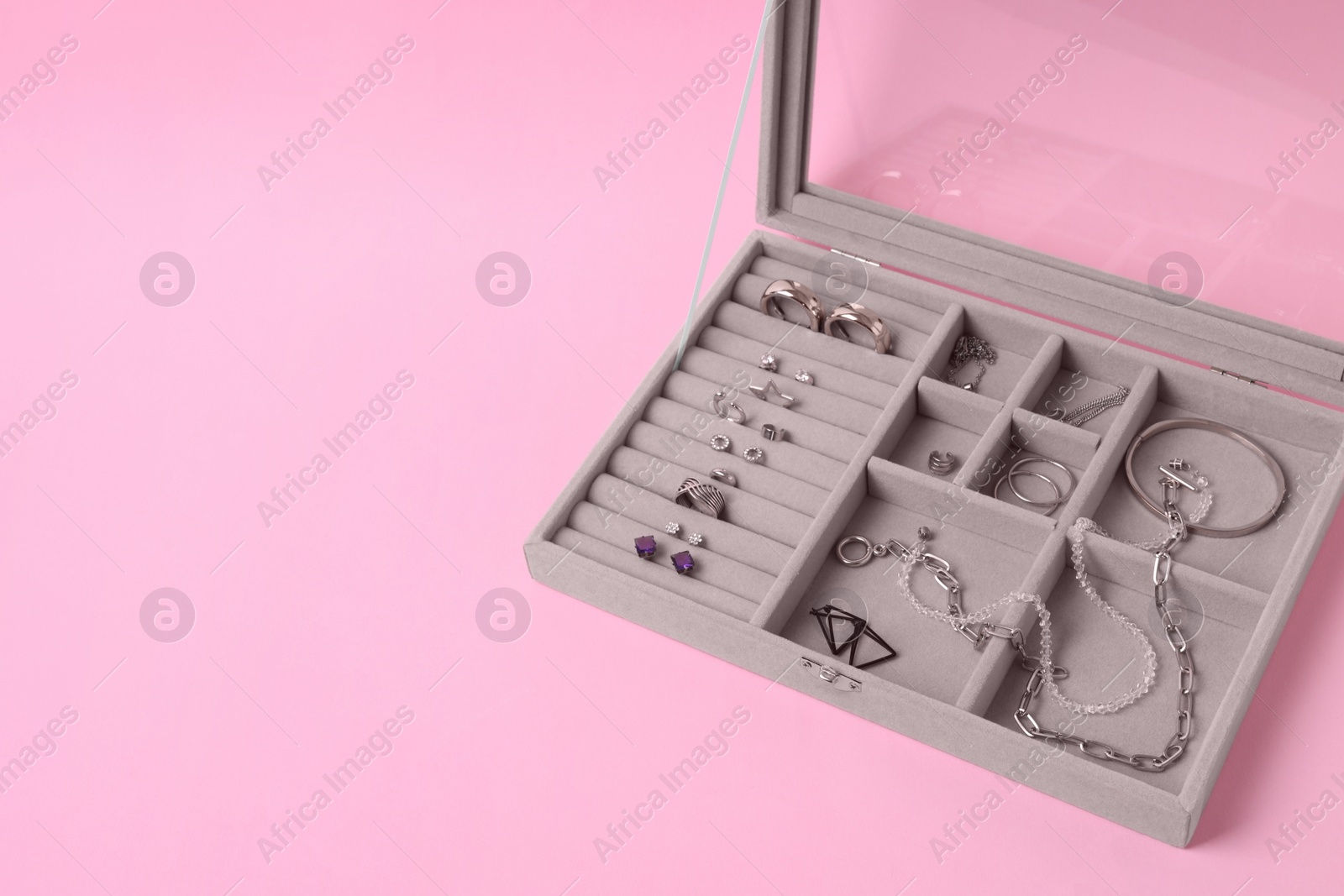 Photo of Jewelry box with many different silver accessories on pink background. Space for text