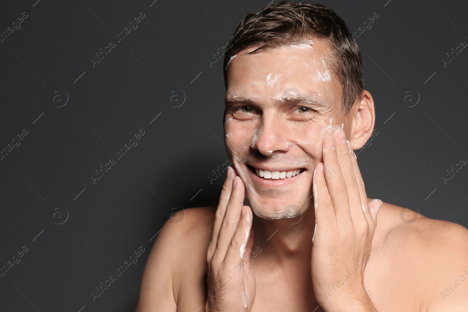 Photo of Man washing face with soap on dark background