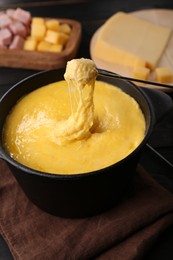 Dipping piece of ham into fondue pot with melted cheese on table, closeup