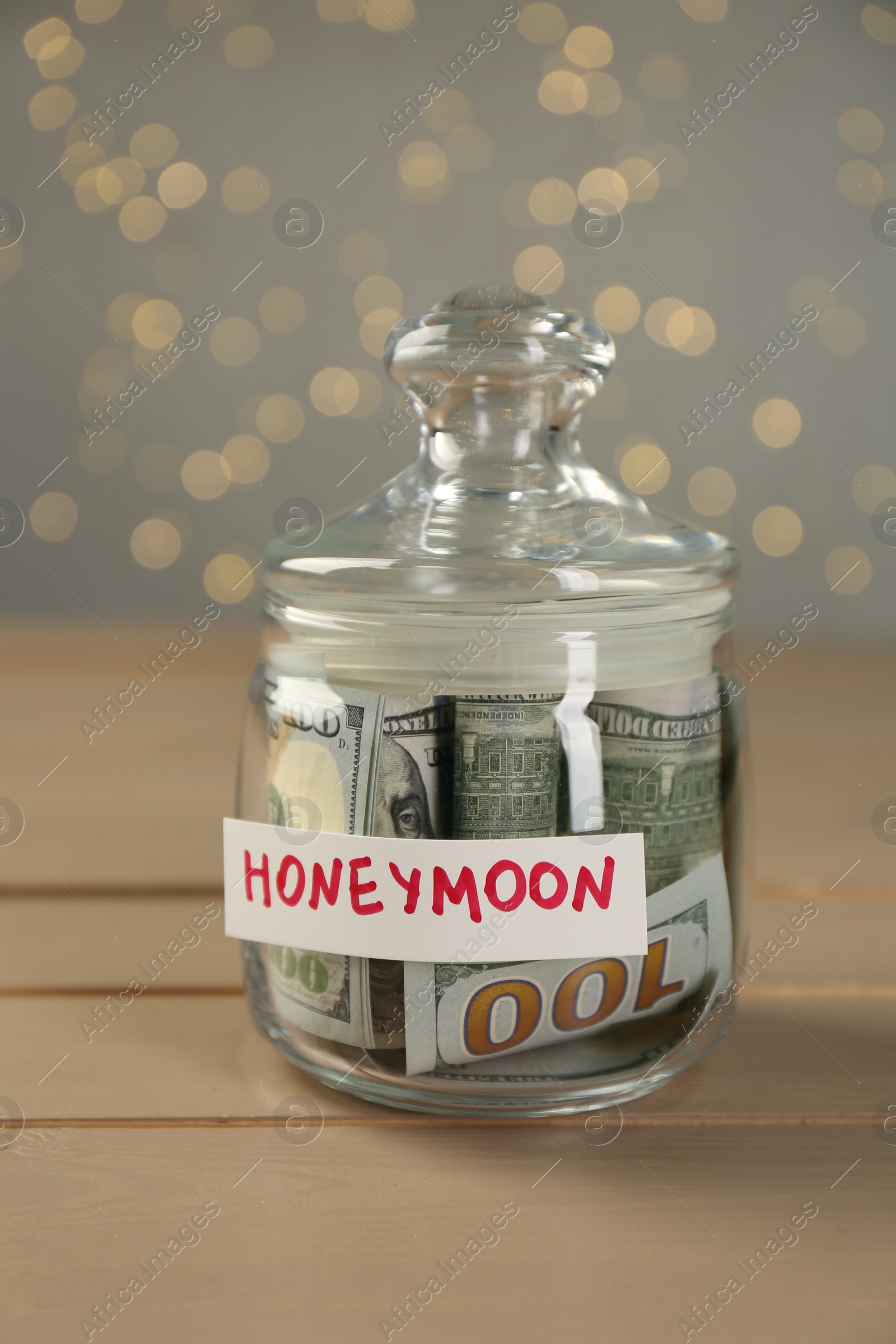 Photo of Glass jar with word Honeymoon and dollar banknotes on wooden table, closeup