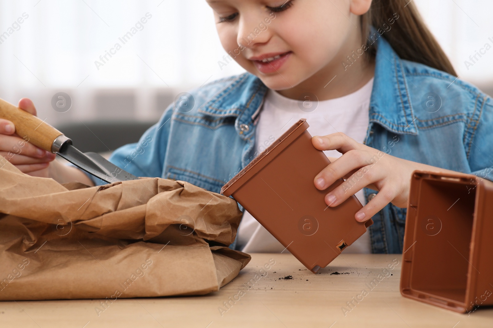 Photo of Cute little girl planting seedling into pot at wooden table indoors, closeup