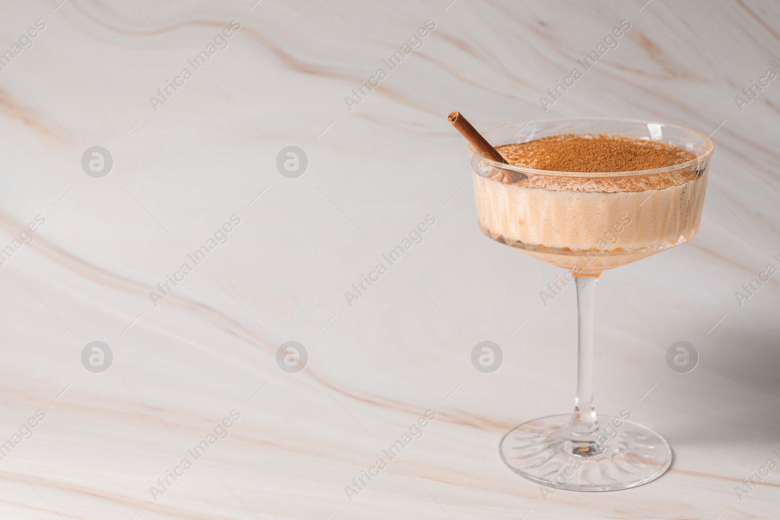 Photo of Delicious eggnog with cinnamon on white marble table. Space for text