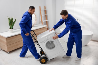 Photo of Male movers carrying washing machine in bathroom. New house