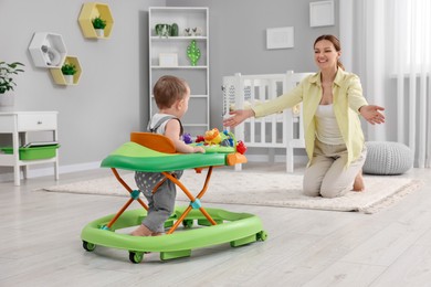 Photo of Mother teaching her little son making first steps with toy walker