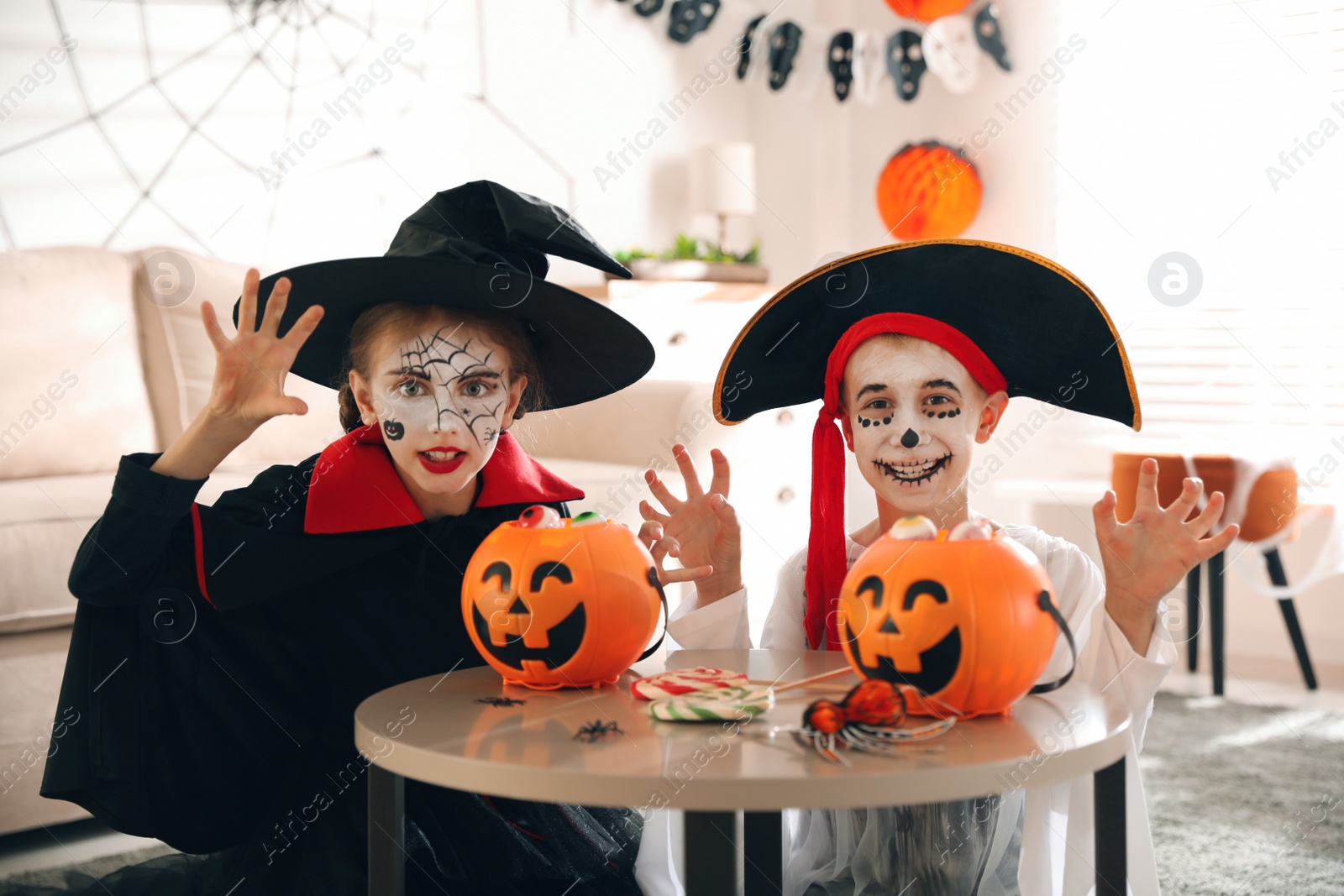 Photo of Cute little kids with pumpkin candy buckets wearing Halloween costumes at home