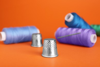 Photo of Thimbles, spools of sewing threads and needle on orange background
