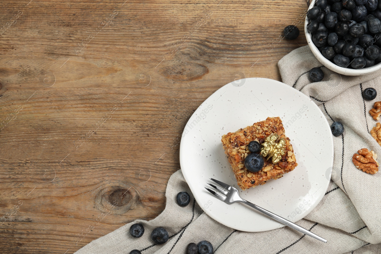 Photo of Piece of delicious layered honey cake with blueberries and nuts served on wooden table, flat lay. Space for text