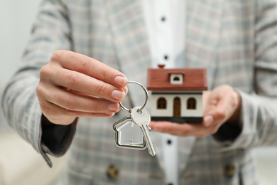 Real estate agent holding house model and key indoors, closeup