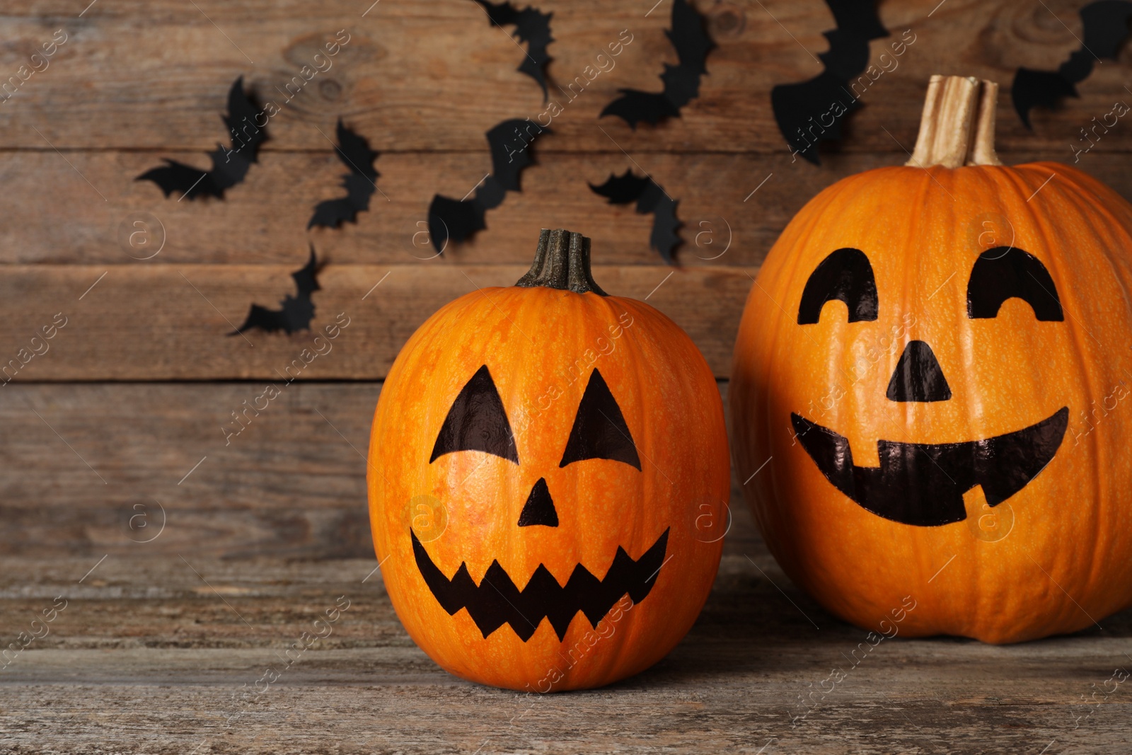 Photo of Pumpkins with drawn spooky faces on wooden table. Halloween celebration