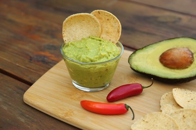 Photo of Delicious guacamole made of avocados with nachos and peppers on wooden table