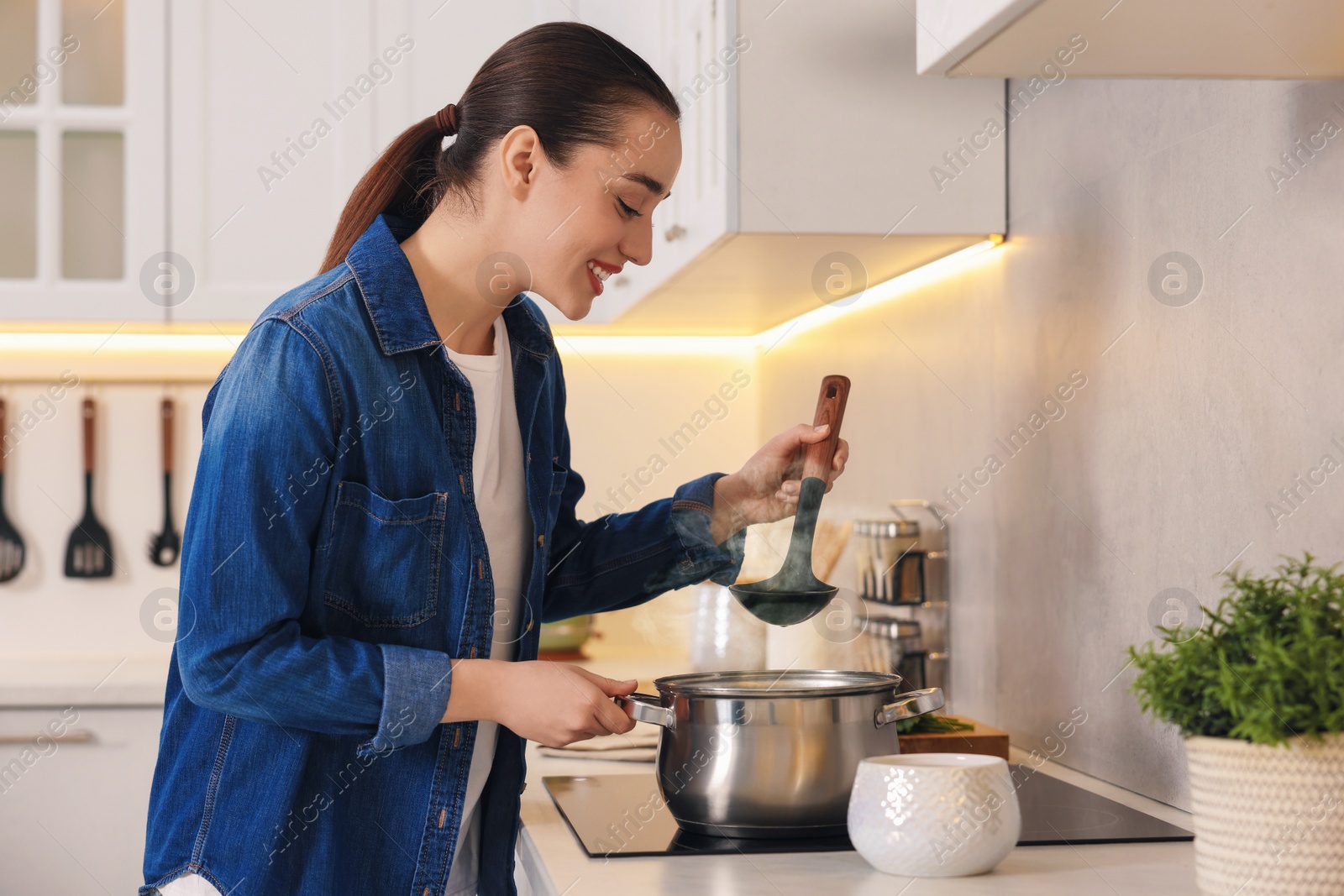 Photo of Smiling woman with ladle cooking soup in kitchen