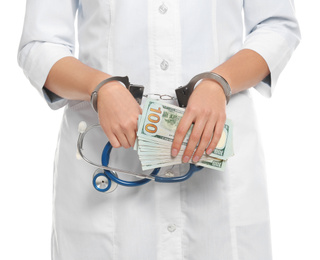 Doctor in handcuffs with bribe and stethoscope on white background, closeup. Corrupted medicine