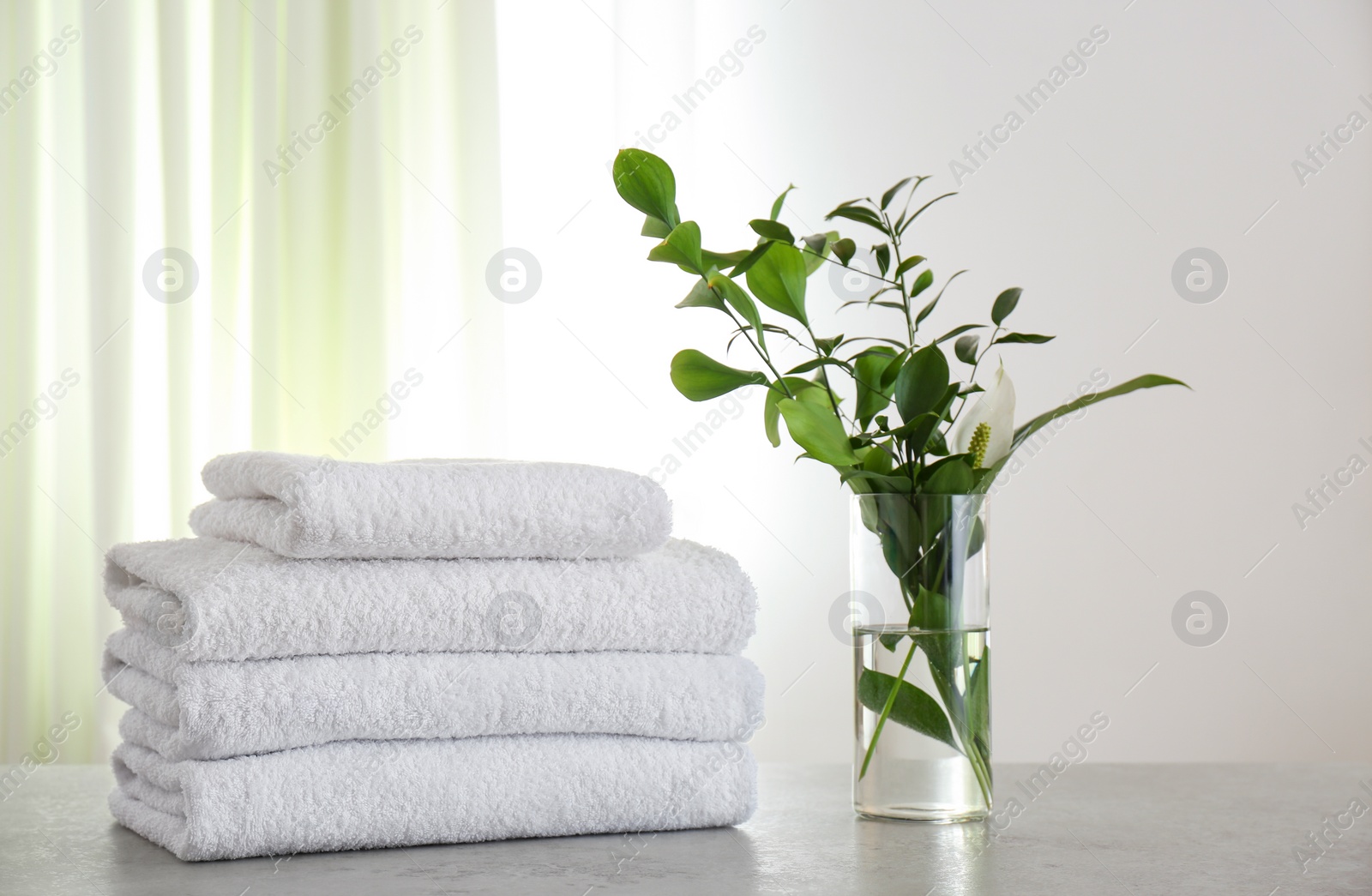 Photo of Fresh towels and green branches on light grey stone table in bathroom