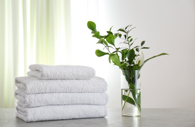 Fresh towels and green branches on light grey stone table in bathroom