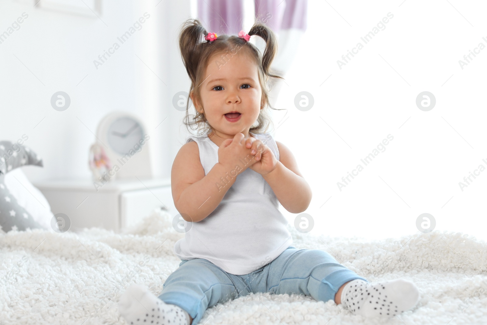 Photo of Adorable little baby girl sitting on bed in room