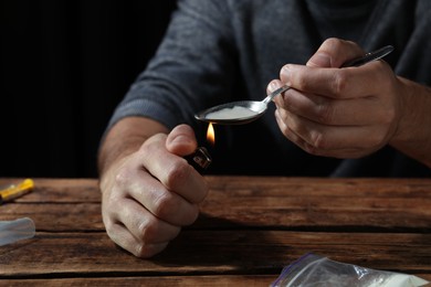 Photo of Man preparing drugs with spoon and lighter at wooden table, closeup