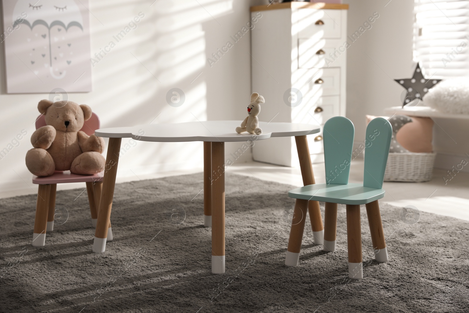 Photo of Small table and chairs with bunny ears in children's room interior