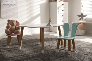 Photo of Small table and chairs with bunny ears in children's room interior