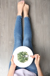 Photo of Young woman with tasty cooked spinach on wooden floor, top view. Healthy food