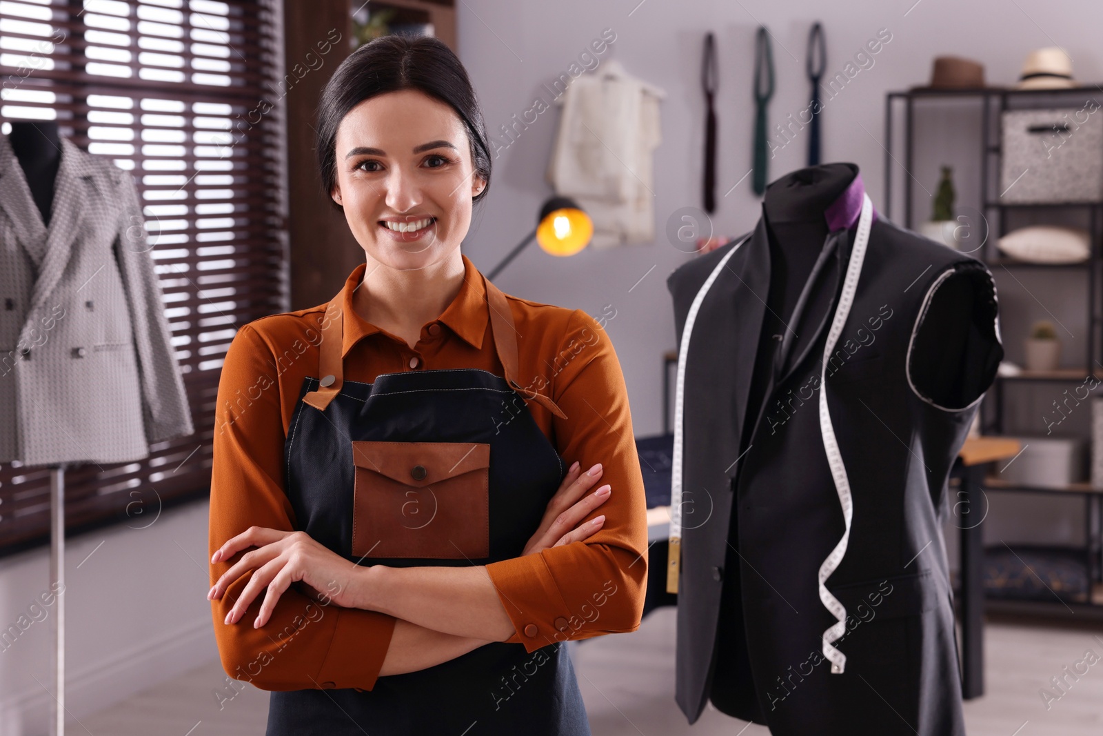 Photo of Happy dressmaker near mannequin with unfinished garment and measuring tape in workshop