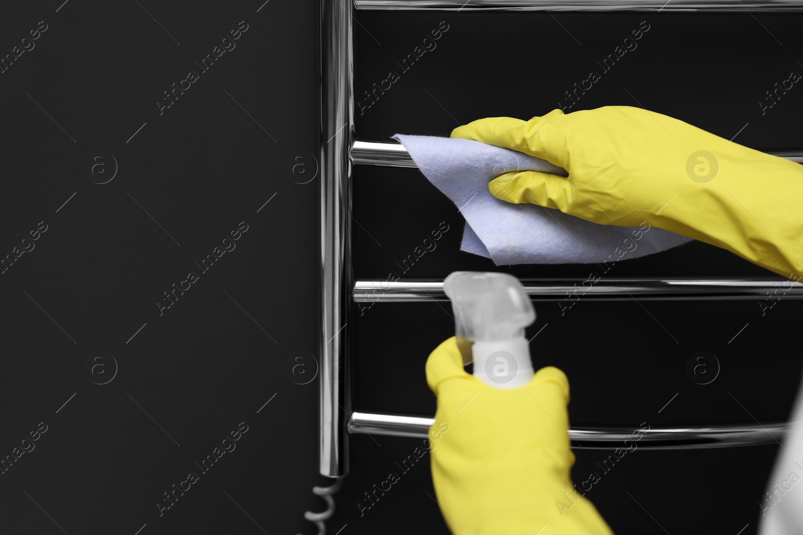 Photo of Woman cleaning heated towel rail with sprayer and rag, closeup