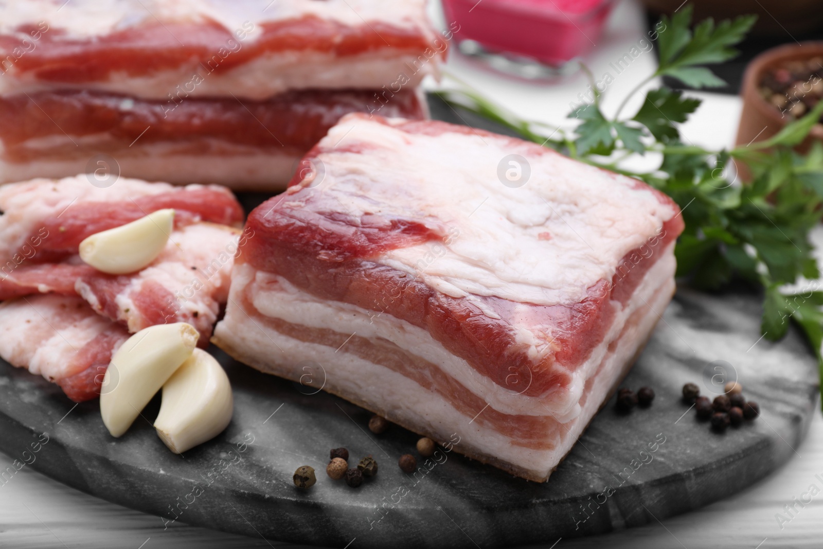 Photo of Pieces of tasty pork fatback with garlic and peppercorns on board, closeup