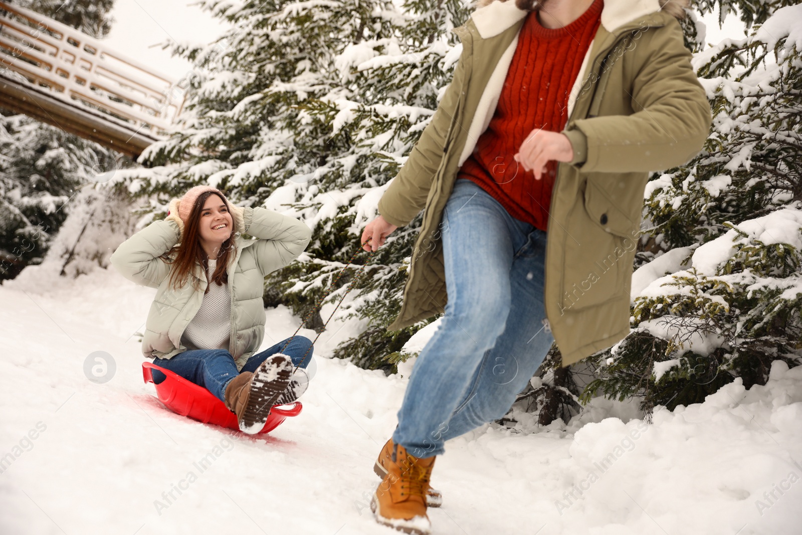 Photo of Young man pulling sled with his girlfriend outdoors on snowy day. Winter vacation