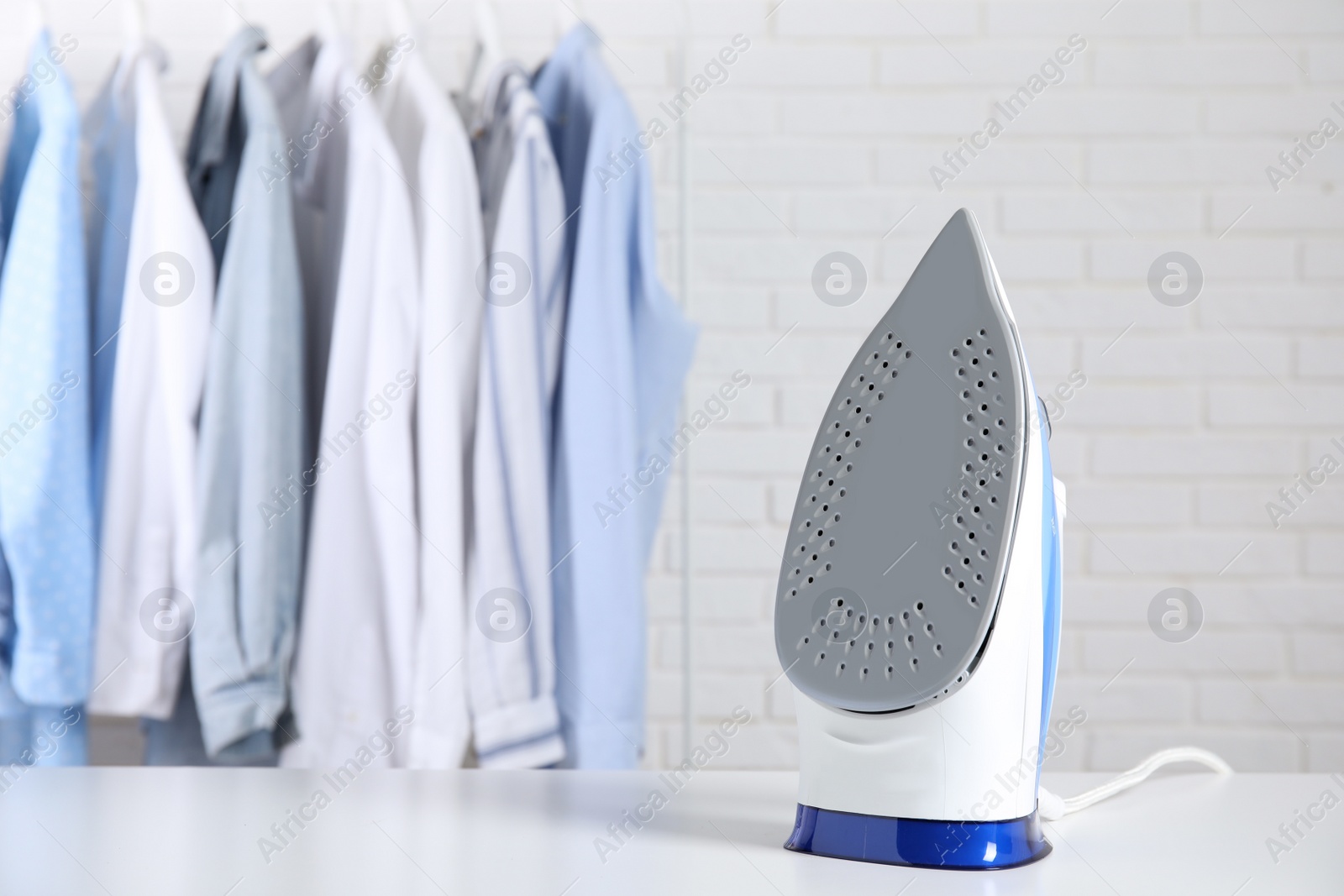 Photo of Modern iron on table near rack with clean clothes indoors, space for text