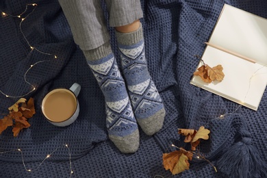 Photo of Woman wearing knitted socks on warm plaid, top view. Cozy season