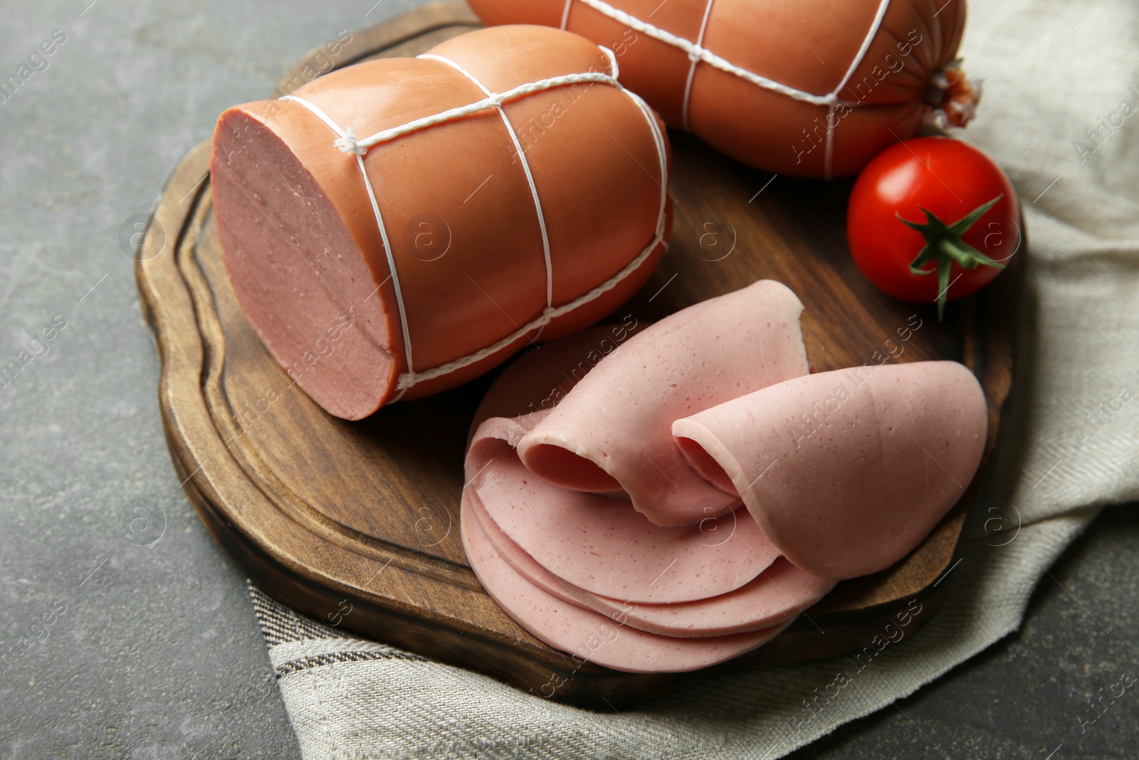 Photo of Board with tasty boiled sausages and tomato on grey textured table, closeup