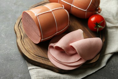 Photo of Board with tasty boiled sausages and tomato on grey textured table, closeup