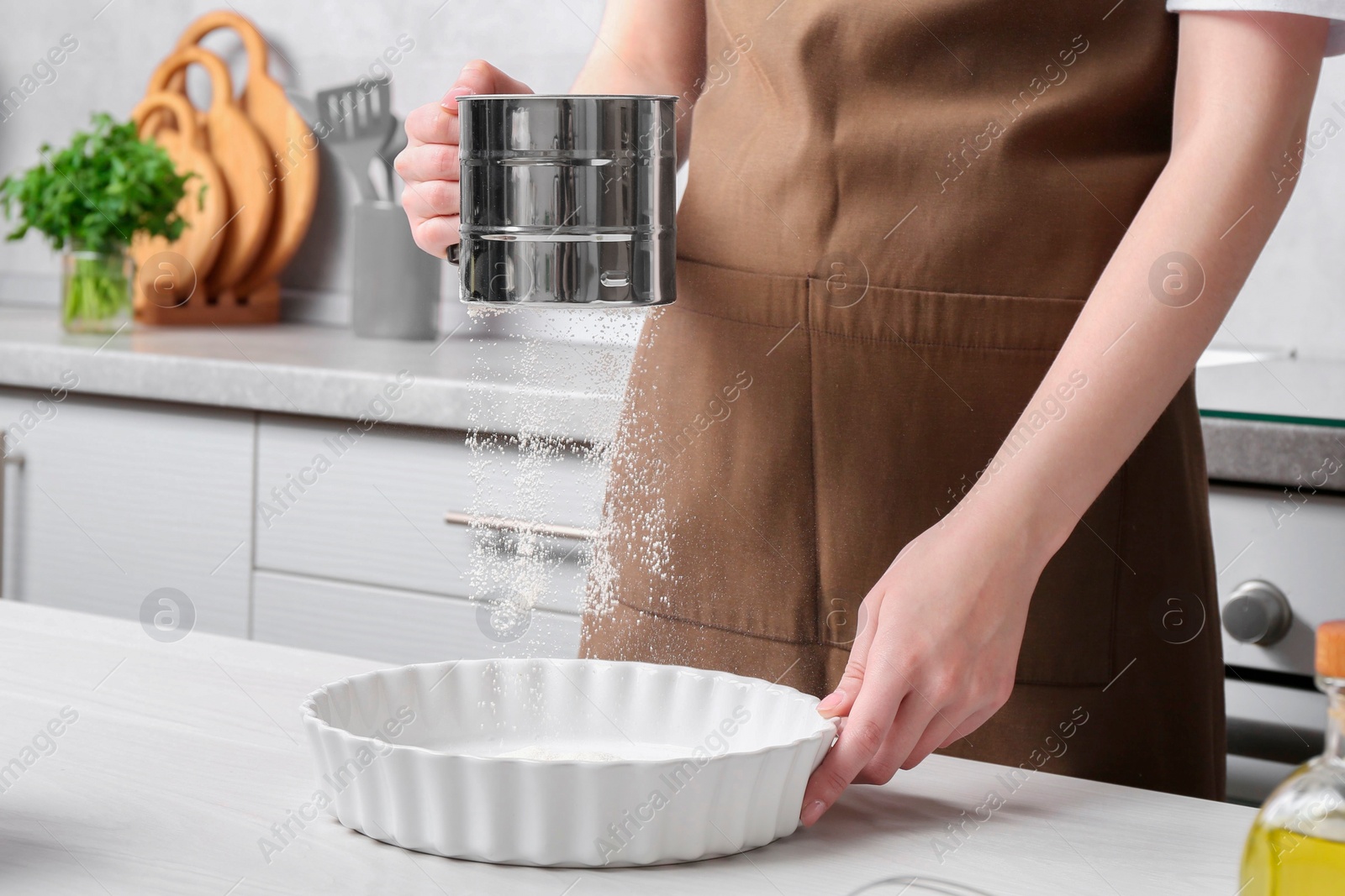 Photo of Woman sieving flour into baking dish at table in kitchen, closeup