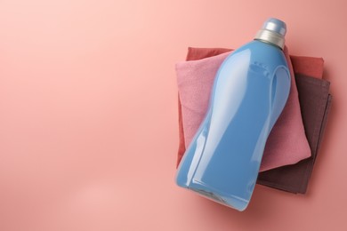 Photo of Bottle of fabric softener and stacked clean clothes on pink background, top view. Space for text