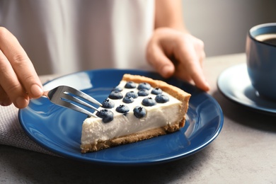 Photo of Woman eating tasty blueberry cake at table, closeup
