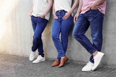 Photo of Group of people in stylish jeans near grey wall outdoors, closeup