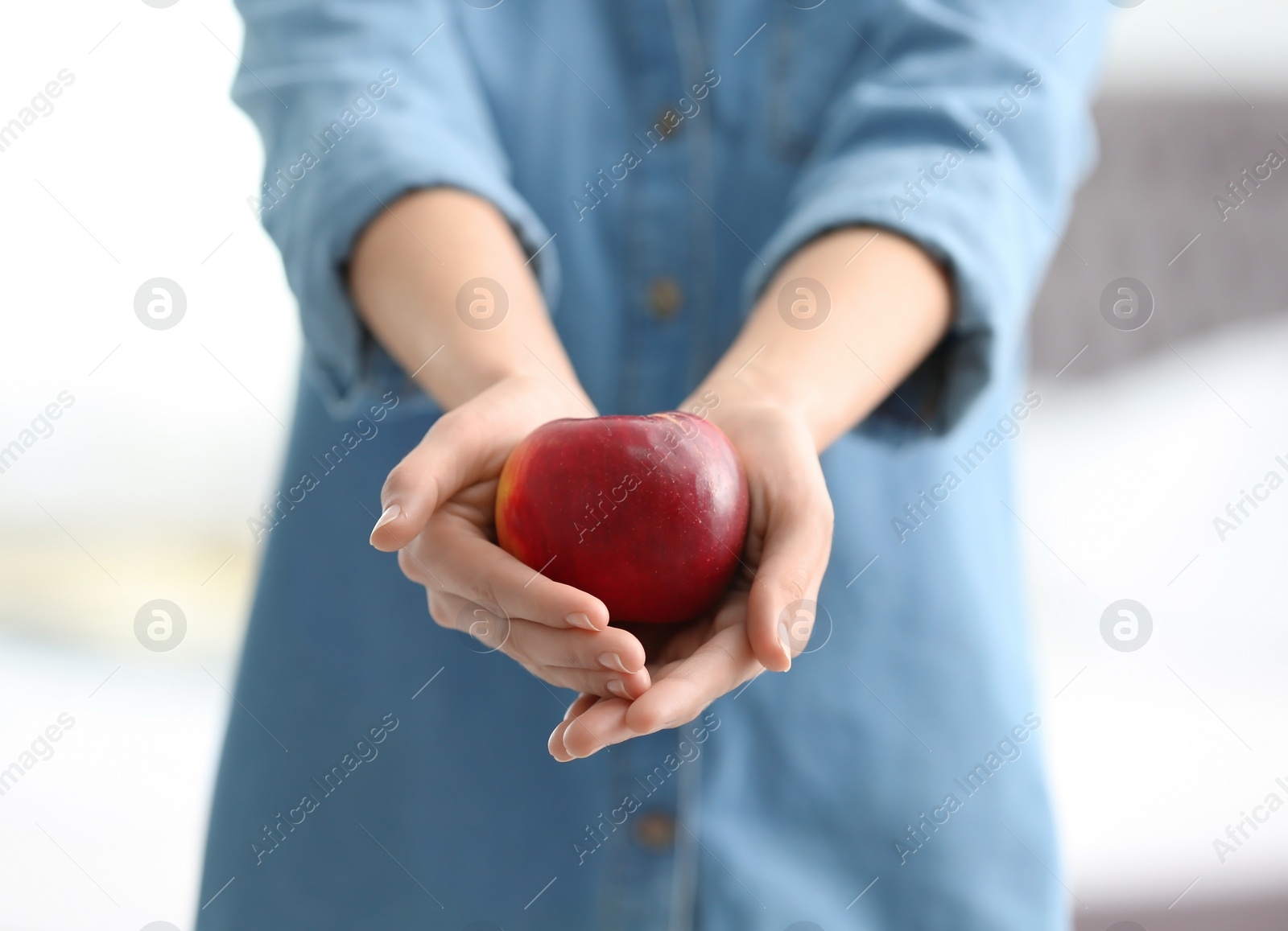 Photo of Woman holding ripe red apple on blurred background, closeup