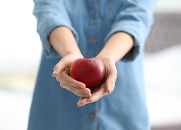 Photo of Woman holding ripe red apple on blurred background, closeup