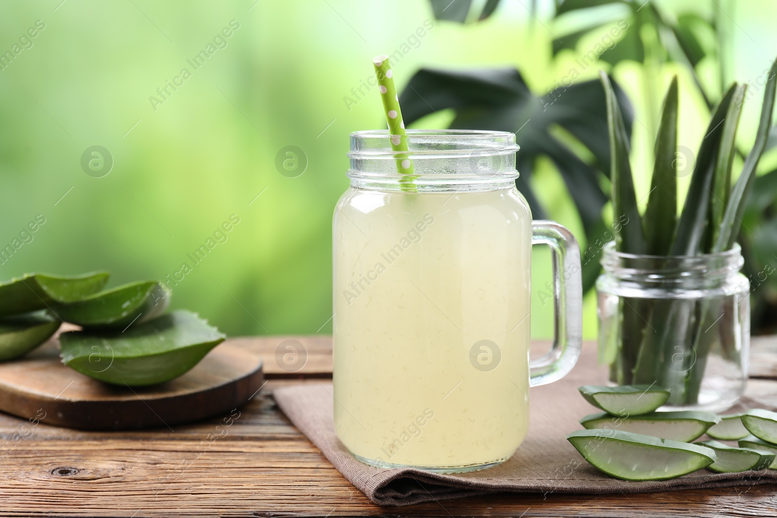 Photo of Fresh aloe juice in mason jar with straw and leaves on wooden table outdoors, closeup