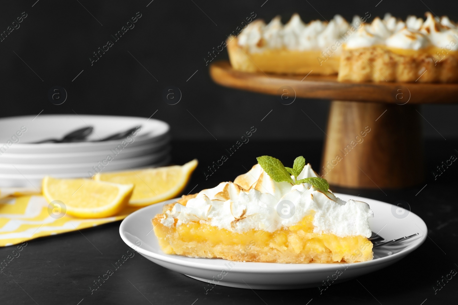 Photo of Plate with piece of delicious lemon meringue pie on black table