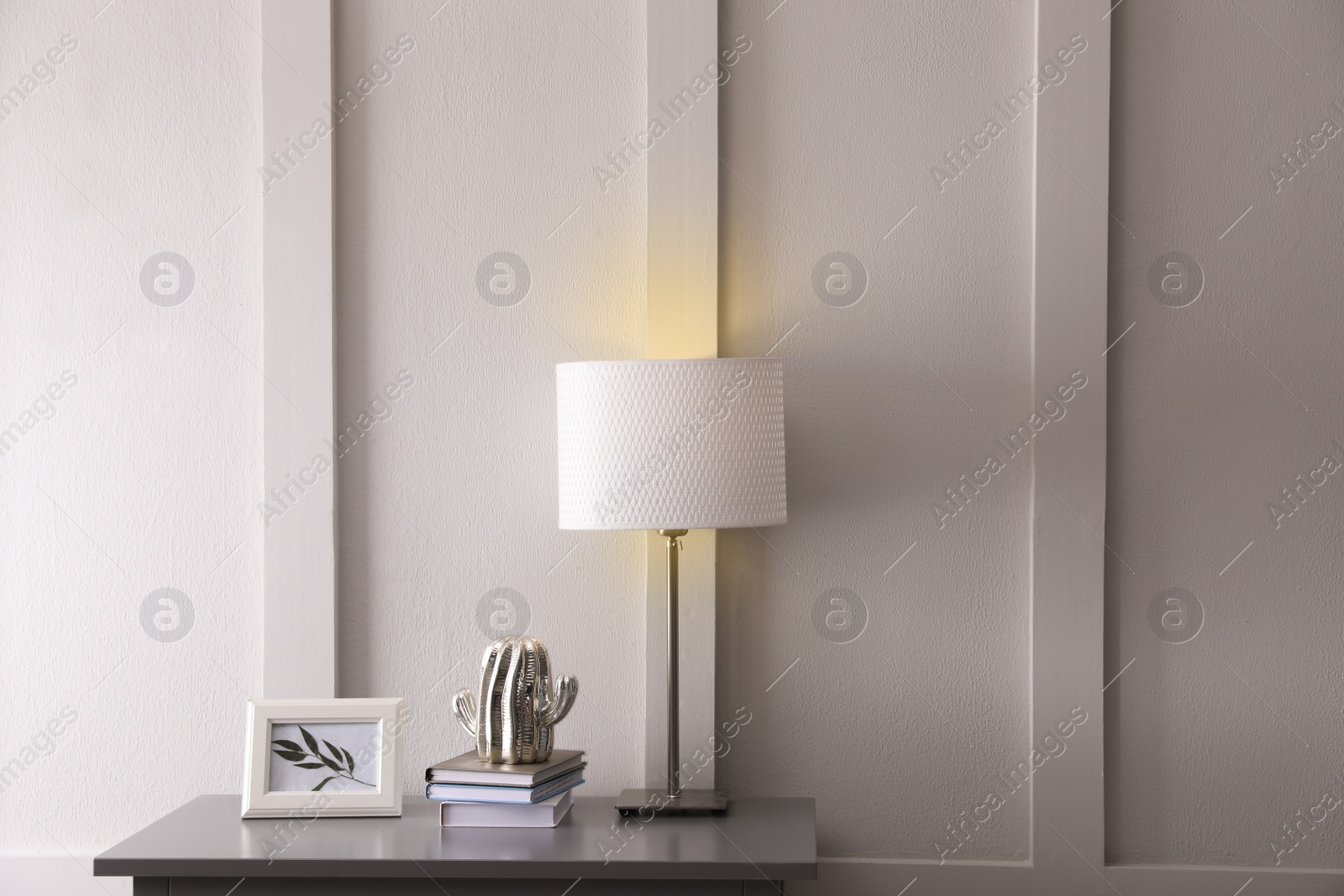 Photo of Wooden table with books, decor and lamp near white wall in room