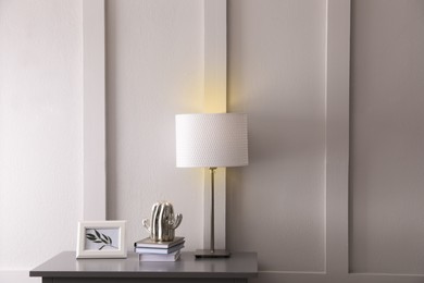 Wooden table with books, decor and lamp near white wall in room